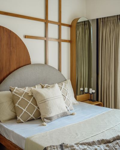 Arched fluted wood headboard with grey bolster and patterned cushions beside an arched mirror and olive curtains