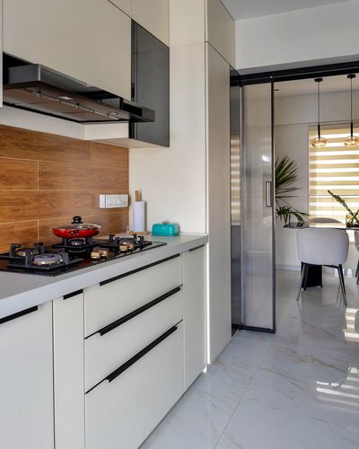 White minimalist kitchen with wood backsplash and reeded glass sliding door to dining area