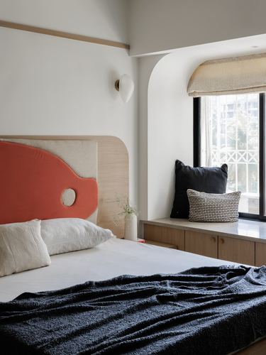Bedroom with coral palette-shaped headboard beside an arched window seat nook