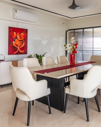 Dining room with cream boucle chairs around a stone-topped table with red runner and Ganesha painting