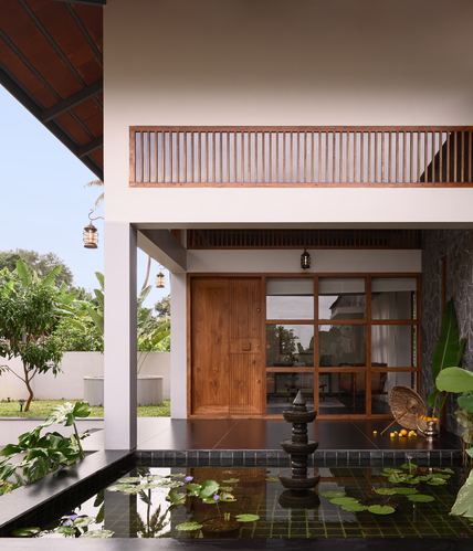 Kerala home entrance with wooden door, louvered balcony, and lotus pond in foreground