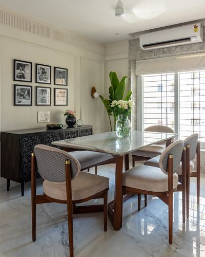Dining room with marble table, teak oval-back chairs, black sideboard and framed photo wall