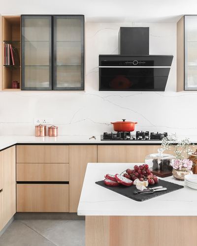 Modern kitchen with wood cabinetry, veined stone counters, black hood, and styled island flatlay