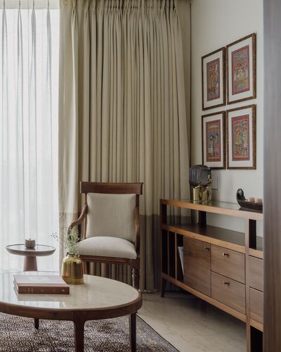 Living room corner with wooden armchair, marble coffee table, and framed miniature art above a wood console