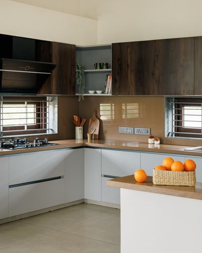 L-shaped modern kitchen with dark wood cabinets, grey base units, and glass backsplash, oranges in basket on island