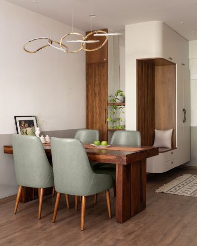 Wooden dining table with sage green chairs beneath a gold ring pendant light