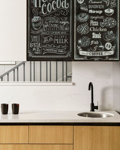 Kitchen counter with chalkboard-illustrated cabinet fronts, black faucet, and marble-look backsplash
