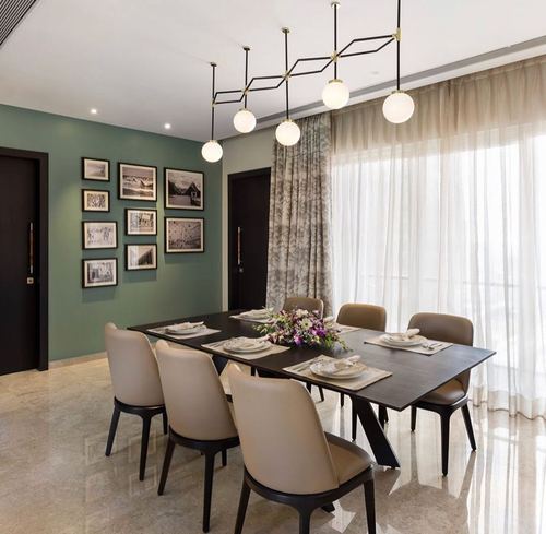 Dining room with sage green gallery wall, dark wood table, cream chairs, and sheer curtains