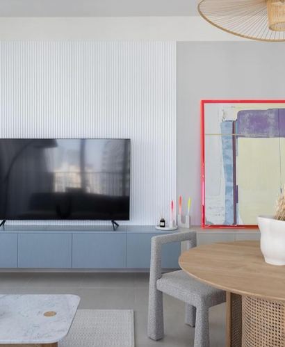 Living room with fluted white wall, blue credenza, TV, and neon-framed abstract art beside dining table
