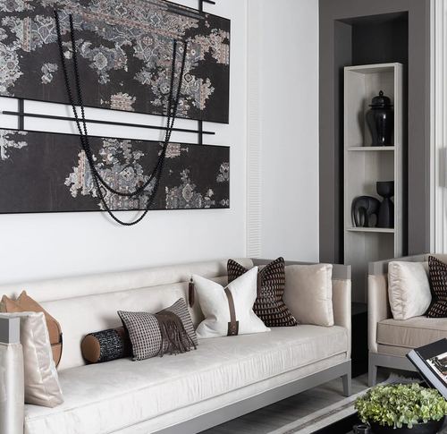 Cream sofa with patterned pillows beneath a large dark tapestry wall art, corner display niche beyond