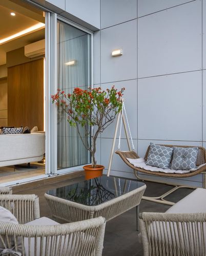 Balcony with wicker swing chair, glass table, and potted bougainvillea beside sliding glass door into living room