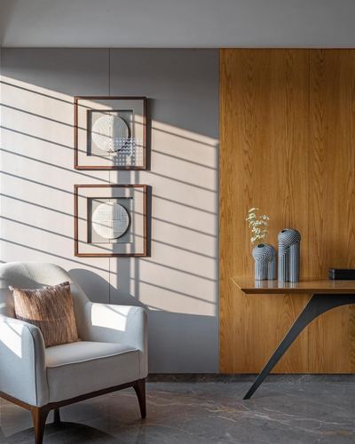 Living room corner with striped light, framed art, cane armchair, and wood-panelled console wall