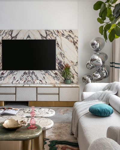 Living room with book-matched marble TV wall, brass console, boucle sofa and chrome sculpture