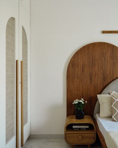 Arched fluted wood headboard beside curved wooden nightstand with flowers, arched cane wardrobe doors on left