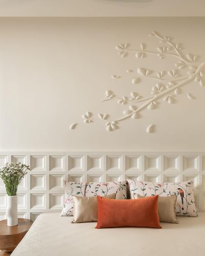 Cream bedroom with sculpted plaster branch wall art above panelled wainscoting and printed pillows