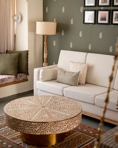 Living room corner with cream sofa, patterned coffee table, and olive paisley wallpaper with framed art.