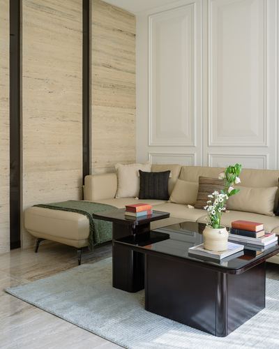 Beige sectional sofa with dark nested coffee tables against a travertine feature wall