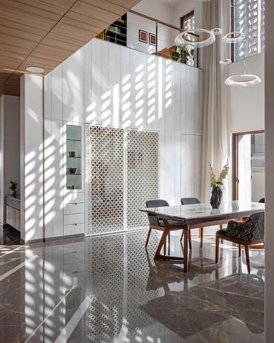 Double-height dining space with jali screen, marble floor, and dappled light patterns