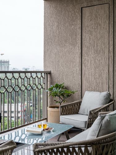 Balcony seating with cane armchairs, glass table, and plant against textured wall overlooking city