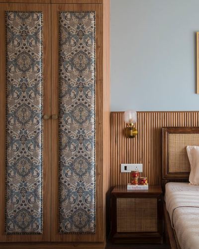 Wardrobe with fabric-paneled doors beside a fluted wood headboard and brass sconce in a bedroom