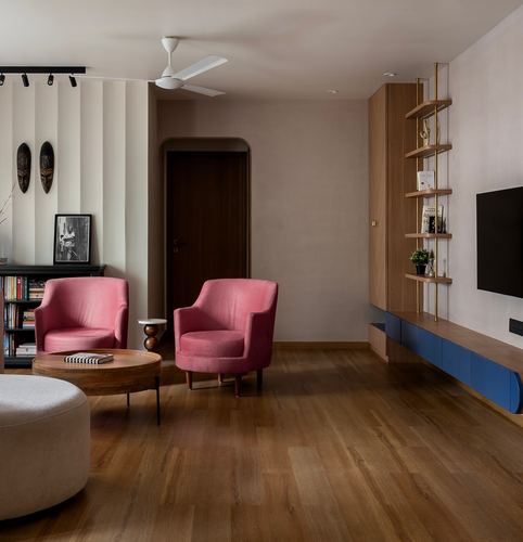 Living room with two pink velvet armchairs, wood floor, and a fluted display shelf beside a TV