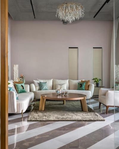 Pink-walled living room with cream channel-tufted sofas, oval wood table, crystal chandelier, striped marble floor
