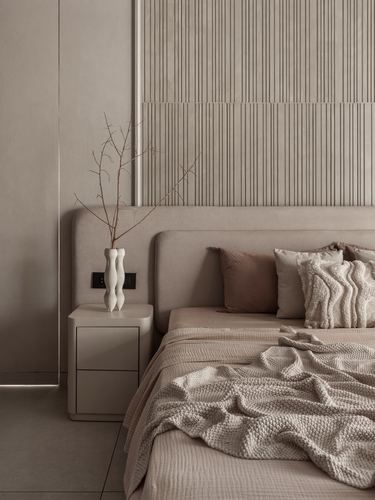 Beige bedroom with curved upholstered headboard, fluted wall panel, and sculptural vase on nightstand