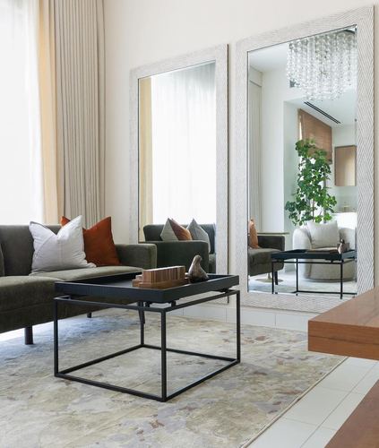 Olive sofa with rust pillows beside two large textured-frame mirrors and a black tray coffee table