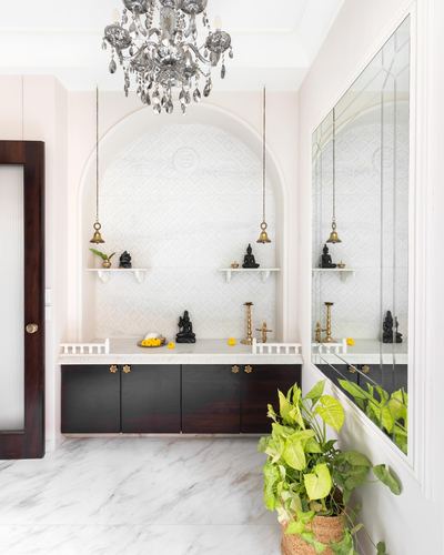 Pooja room with arched textured niche, hanging bells, chandelier, and dark wood cabinetry under marble counter