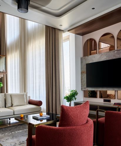 Living room with rust boucle armchairs, cream sofa, and arched openings above a stone tv wall