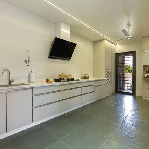 Long white galley kitchen with black chimney hood, sage green tiled floor, and glass door at end