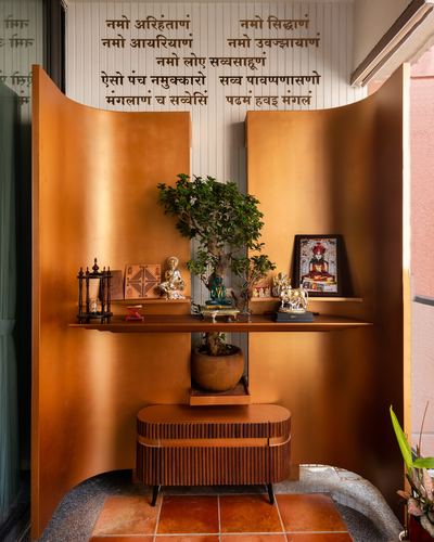 Pooja nook with curved brass panels, floating shelf holding idols and a bonsai, terracotta floor.