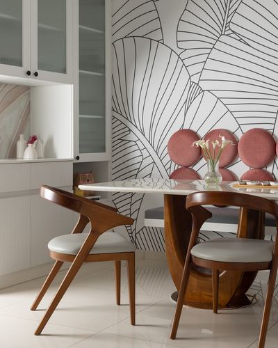 Dining nook with carved wood chairs, marble-top table, and pink round-back banquette against leaf-print wallpaper
