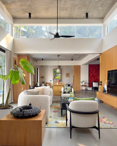 Open-plan living room with double-height windows, wood cabinetry, boucle armchairs, and a floral rug