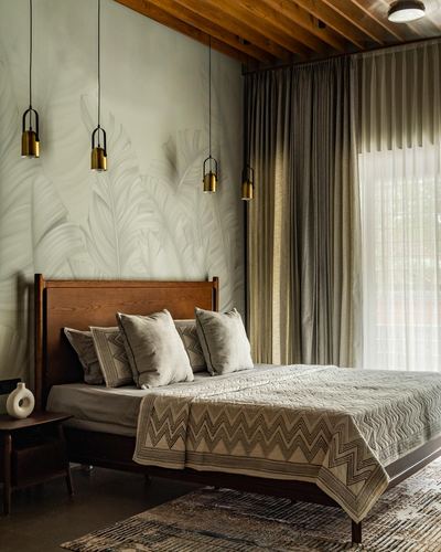 Bedroom with wooden headboard, brass pendant lights over botanical mural wall, and layered linen bedding