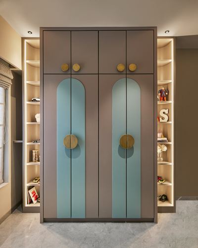 Mauve wardrobe with arched blue panels and brass handles flanked by lit display shelves