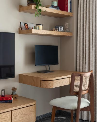 Wall-mounted wooden desk with monitor beneath floating shelves and a cane-back chair