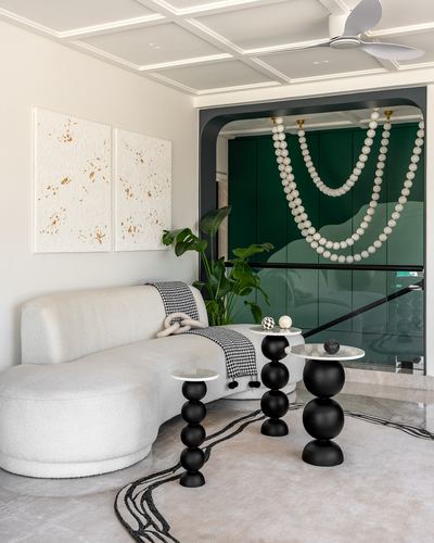 Curved white boucle sofa beside black orb side tables and a beaded chandelier over a green glass wall