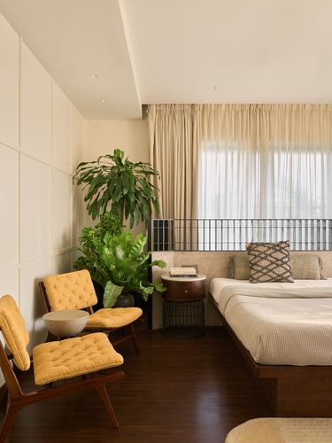 Bedroom corner with mustard tufted chairs, large plant, and platform bed behind a metal grille screen