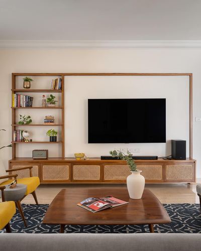 Living room with wood TV unit, cane cabinet fronts, open bookshelf, yellow chairs and wooden coffee table