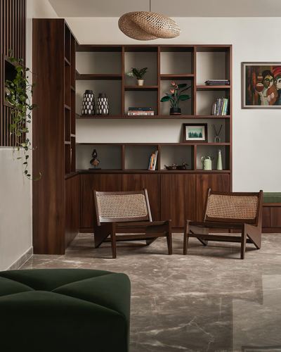 Wooden shelving unit with curated objects above two cane lounge chairs on a stone floor