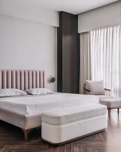 Bedroom with pink fluted headboard bed, white bench, cane chair by curtained window, wood floor