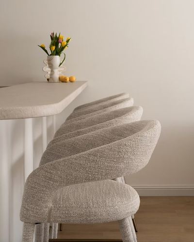 Row of curved boucle bar stools beside a pale stone counter with a vase of tulips