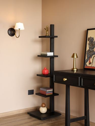 Black ladder shelf with curios beside sconce and console desk with lamp and artwork