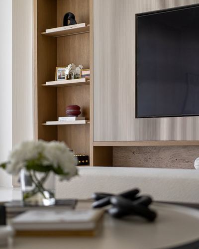Living room shelving niche with decor beside wall-mounted tv on ribbed panel wall, upholstered bench below.