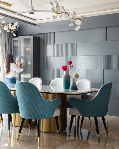 Dining room with teal velvet chairs around marble table and fluted grey wall panel