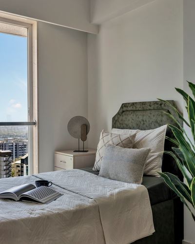 Bedroom with sage upholstered headboard, layered pillows, and floor-to-ceiling window with city view