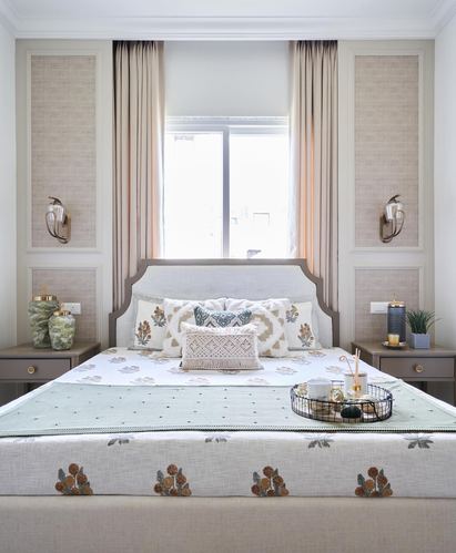 Symmetrical bedroom with upholstered headboard, panelled walls, sconces and floral-embroidered bedding.