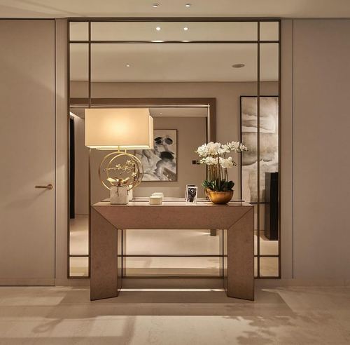 Entryway console with lamp, orchids, and gridded mirror in a neutral penthouse foyer