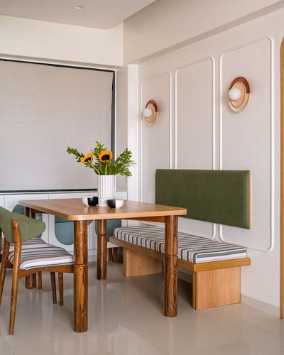 Dining nook with wooden table, striped bench, green velvet banquette, and paneled wall sconces